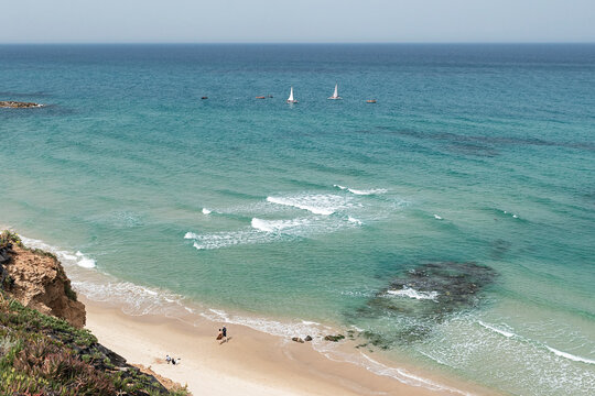 looking down from the cliff onto the eastern Mediterranean Beach at Netanya in Israel with people on the beach and small boats sailing in the sea