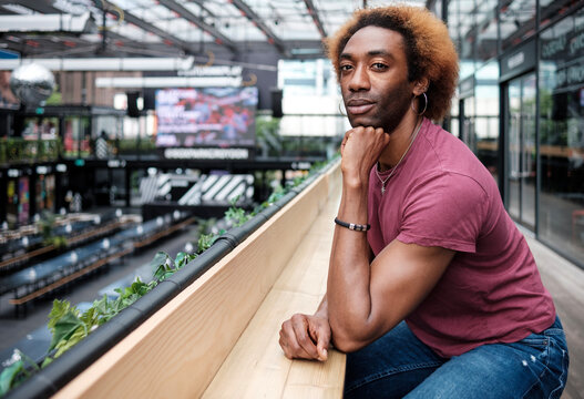 Young non-binary person sitting on a table and looking at camera. He is in an empty mall.