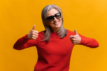 Glad middle-aged gray-haired woman in sunglasses smiling, showing big fingers, gesturing...