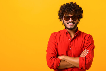 Fototapeta na wymiar Portrait of happy satisfied handsome young man in shirt standing with crossed arms and looking at camera with toothy smile. Indoor studio shot on orange background