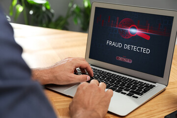 Fraud prevention security system. Man using laptop at wooden table, closeup