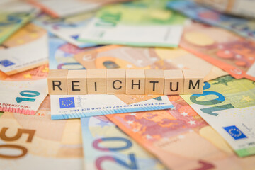Das Wort Reichtum – in deutsch für rich -  auf Geldscheine Euro Euroscheine mit Holzwürfel...