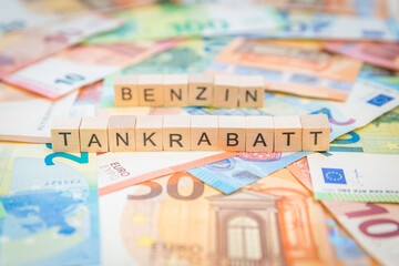Das Wort Tankrabatt – in deutsch für Fuel discount -  und Benzin – in deutsch für Gasoline -  im Hintergrund auf Geldscheine Euro Euroscheine mit Holzwürfel geschriebener Text