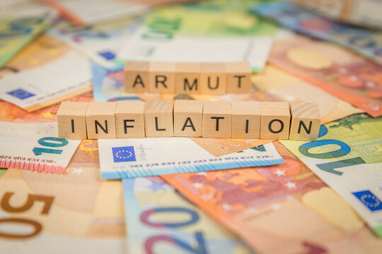 Das Wort Inflation und Armut – in deutsch für poor -  im Hintergrund auf Geldscheine Euro Euroscheine mit Holzwürfel geschriebener Text