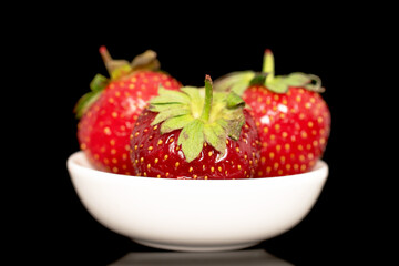 Three berries of ripe organic strawberries on a white ceramic saucer, close-up, isolated on a black background.