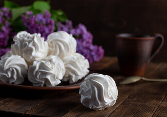 apple marshmallow on a wooden background in a plate, in the background - a cup of coffee, lilac branches. French village morning over a cup of coffee with delicate marshmallows. rustic style