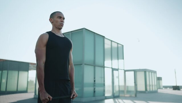 Bald serious sportsman wearing black T-shirt doing sport exercises with an elastic band outdoors in the morning