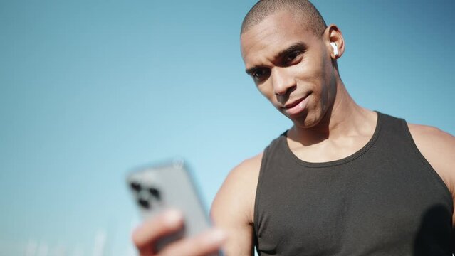 Bald pleased sportsman wearing black T-shirt typing on phone outdoors in the morning