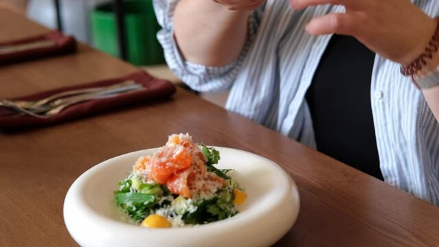 Woman takes picture of avocado and salmon salad on smartphone in restaurant close-up. Slow motion