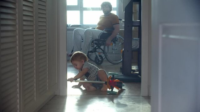 Father in a wheelchair watching his little baby trying