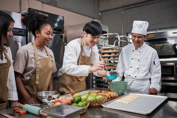 Fototapeta na wymiar Cuisine course, senior male chef in uniform teaches young cooking class students, brushes pastry dough with eggs cream, prepares ingredients for bakery foods, fruit pies in stainless steel kitchen.