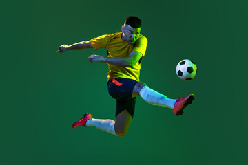 Fototapeta na wymiar Studio shot of young professional male football soccer player in motion isolated on green background in neon. Concept of sport, goals, competition, hobby, achievements