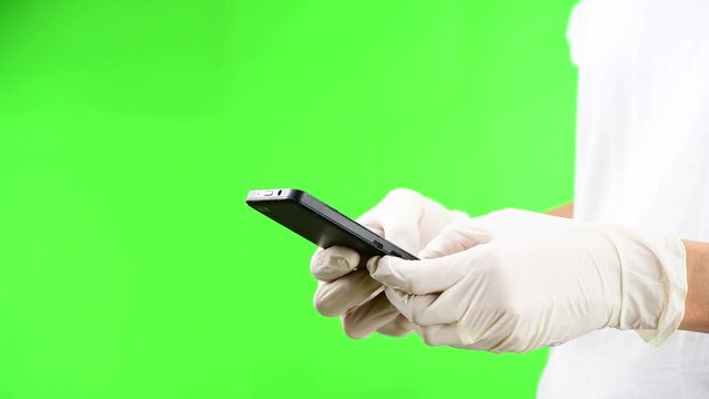 Woman texting with her smartphone with protective white latex gloves against large green background and with large copy space