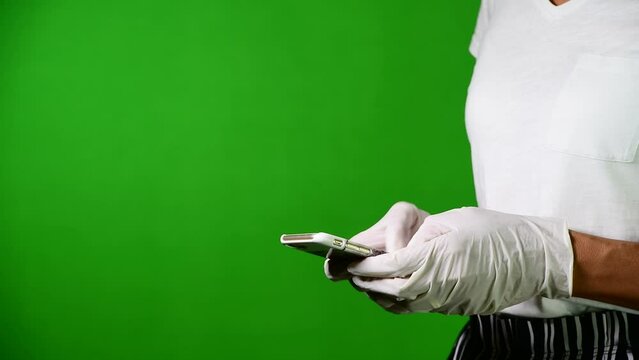 Woman texting with her smartphone with protective white latex gloves against large green background and with large copy space