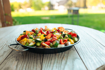  Grilled vegetables in a pan on a wooden table in the backyard of the house at summer time. Vegan, vegetarian, seasonal, summer eating concept. 