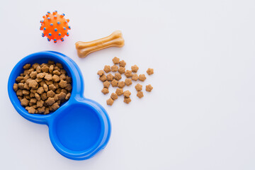 top view of bone shaped pet treat near bowl with dry pet food and rubber toy isolated on white.