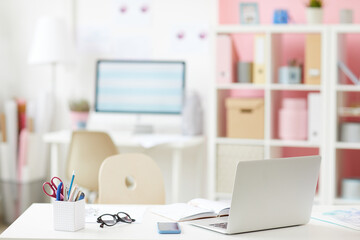 Modern office desk with devices and supplies in cozy room with shelves in background