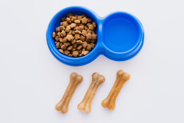 top view of bone shaped pet treats near bowl with water and dry pet food isolated on white.
