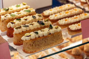 Eclairs on the shelf of a pastry shop or cafe. Tasty french sweets on window shop, delicious pastries for coffee. Cakes in pastry shop, variety of desserts with creamy topping on display in bakery