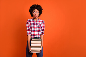 Photo of impressed confused girl hold stack book supplies open mouth isolated on orange color...