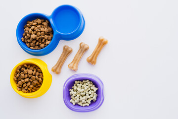 top view of bone shaped pet treats near bowls with water and dry pet food isolated on white.