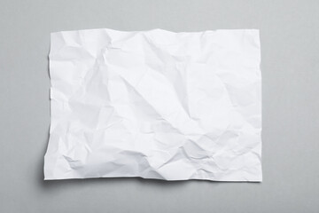 Sheet of white crumpled paper on grey background, top view