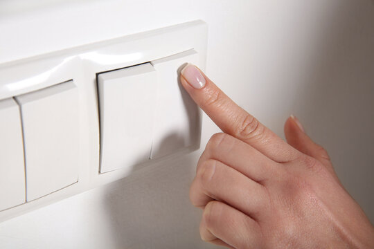 Woman turning off light switch indoors, closeup. Energy saving concept