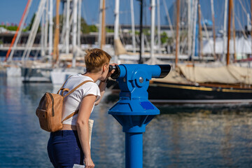 Woman use binoscope in the Barcelona port. Blue city binocular, telescope for town view