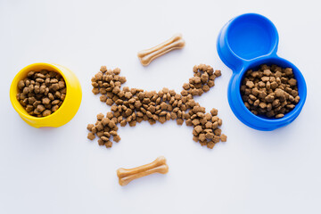 top view of bone shape made of dry pet food near bowls isolated on white.