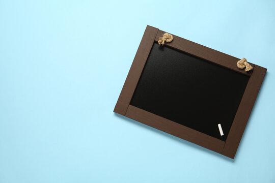 Clean small blackboard with piece of white chalk on light blue background, top view. Space for text