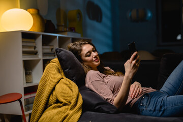 woman relaxing on sofa and texting messages on smartphone. evening night scene