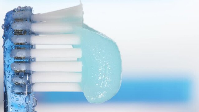 Toothbrush and toothpaste. Vertical macro view of blue toothbrush with water drops on which toothpaste is squeezed on blue-white background with copy space. Slow motion