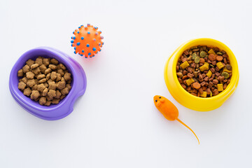 top view of different dry food for pets in bowls near toys isolated on white.