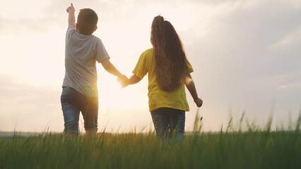 children walking a in the park. boy and girl friendship are holding hands walking on the grass in the park at sunset. happy family in nature outdoors. children holding hands at sunset happy family