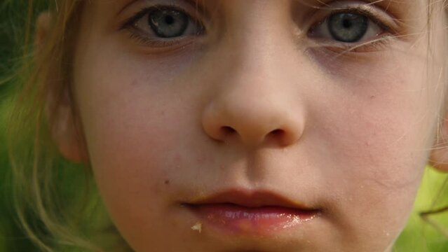 A close-up of the face of a beautiful girl with big blue eyes in a city park. The child's mouth is stained with ice cream. Carefree happy childhood
