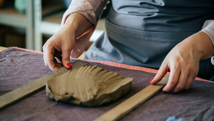 Close Up Photo Of Woman Hands Molding Clay At Her Workshop. 
Small Business: Unrecognizable woman potter holding two clay slats and making ceramics on a desk in her studio.