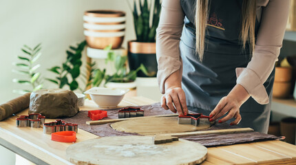 Close Up Photo Of Woman Hands Making Christmas Ornaments Of Clay At Her Studio.
Unrecognizable woman artisan using cookie cutters in star shape for handmade Christmas decoration at her workshop desk.