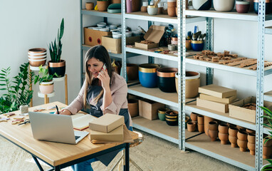Happy Woman Potter In Talking On A Mobile Phone With Customer While Preparing Packages For Shipping...