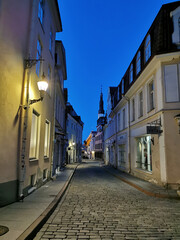 A narrow cobbled street in the Old City, at the end of which you can see the spire of the Church of the Holy Spirit against the blue sky. Old Tallinn.