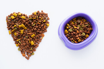 top view of heart made of crunchy dry pet food and plastic bowl isolated on white.