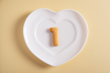 Biscuits forming number 1 on the white plate and yellow light background