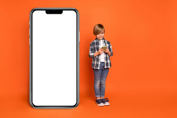 Full length photo of young boy use mobile button app website digital isolated over orange color background