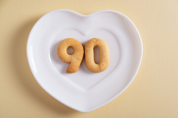 Biscuits forming number 90 on the white plate and yellow light background