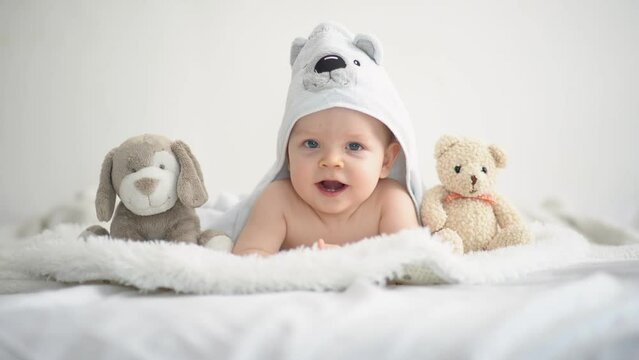 Cute funny little baby boy with toys, relaxing in bed after bath, laughing happily