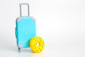 Obraz premium A blue suitcase on wheels and a yellow inflatable donut stand on a white background.