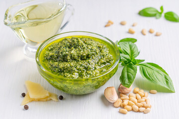 Italian homemade herbal pesto sauce made of blended parmesan cheese, green basil leaves, pine nuts, garlic, black pepper and olive oil served in glass bowl on white wooden background used on pasta