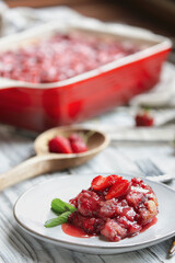 Sweet homemade strawberry cobbler or Sonker baked in a red ceramic pan over a rustic white wood table. Extreme selective focus with blurred background.