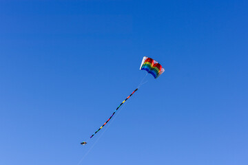 Colorful rainbow kite with tail flying in blue sky