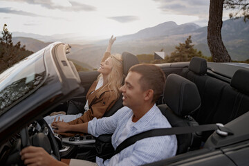 Happy couple in love roofless convertible car holding hands driving by the mountain road, side view