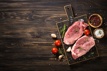 Fresh meat steaks, pork steaks with herbs and spices on craft board at wooden background. Top view...
